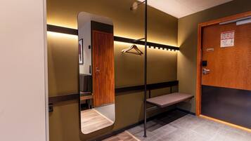 A hotel lobby with a wooden bench, a coat rack, a mirror, and a door with a sign.