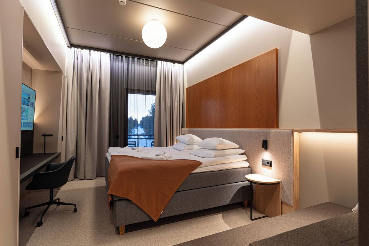 A modern hotel room with a bed, a desk, a chair, and a nightstand.