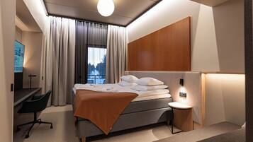 A modern hotel room with a bed, a desk, a chair, and a nightstand.