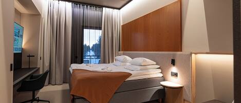 A modern hotel room with a bed, a desk, a chair, and a nightstand.
