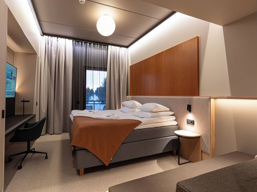 Una habitación de hotel moderna con una cama, un escritorio, una silla y una mesita de noche.