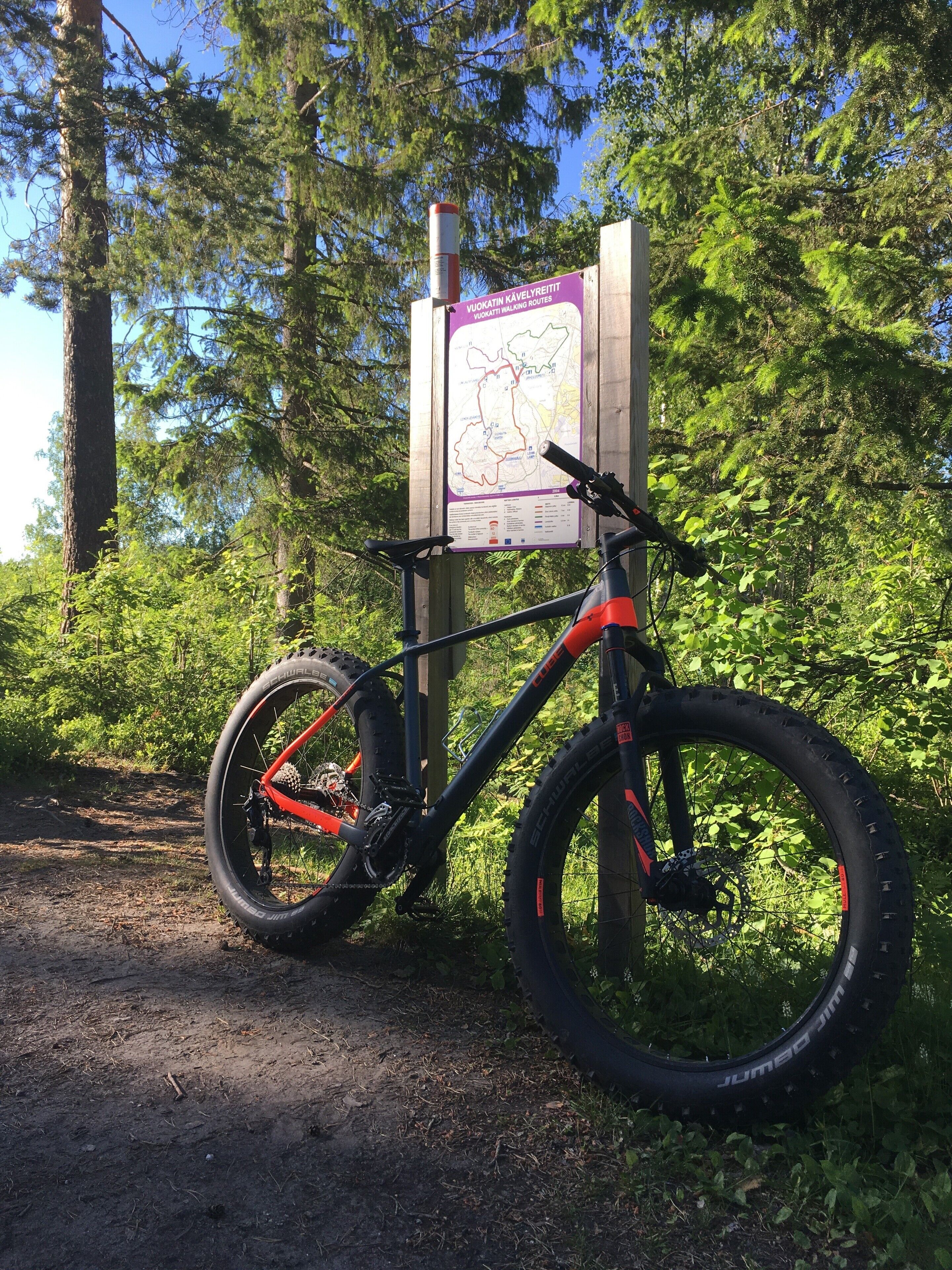 A mountain bike parked next to a trail map sign in a forested area.