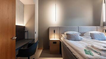 Quarto de hotel moderno com escrivaninha de madeira, cama confortável com almofadas e mesa de cabeceira com abajur.