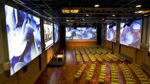 A conference room with rows of green chairs and large screens displaying floral images. - Hotel Lasaretti (Oulu)
