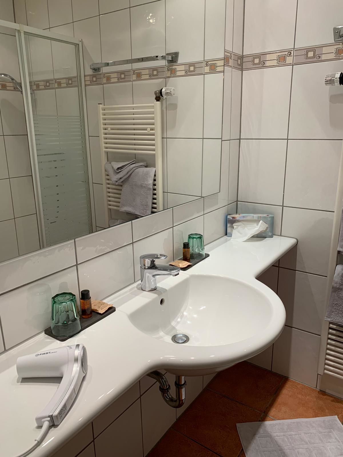 Ein modernes Badezimmer mit einem großen weißen Waschbecken, einem Spiegel und einem Handtuchhalter.