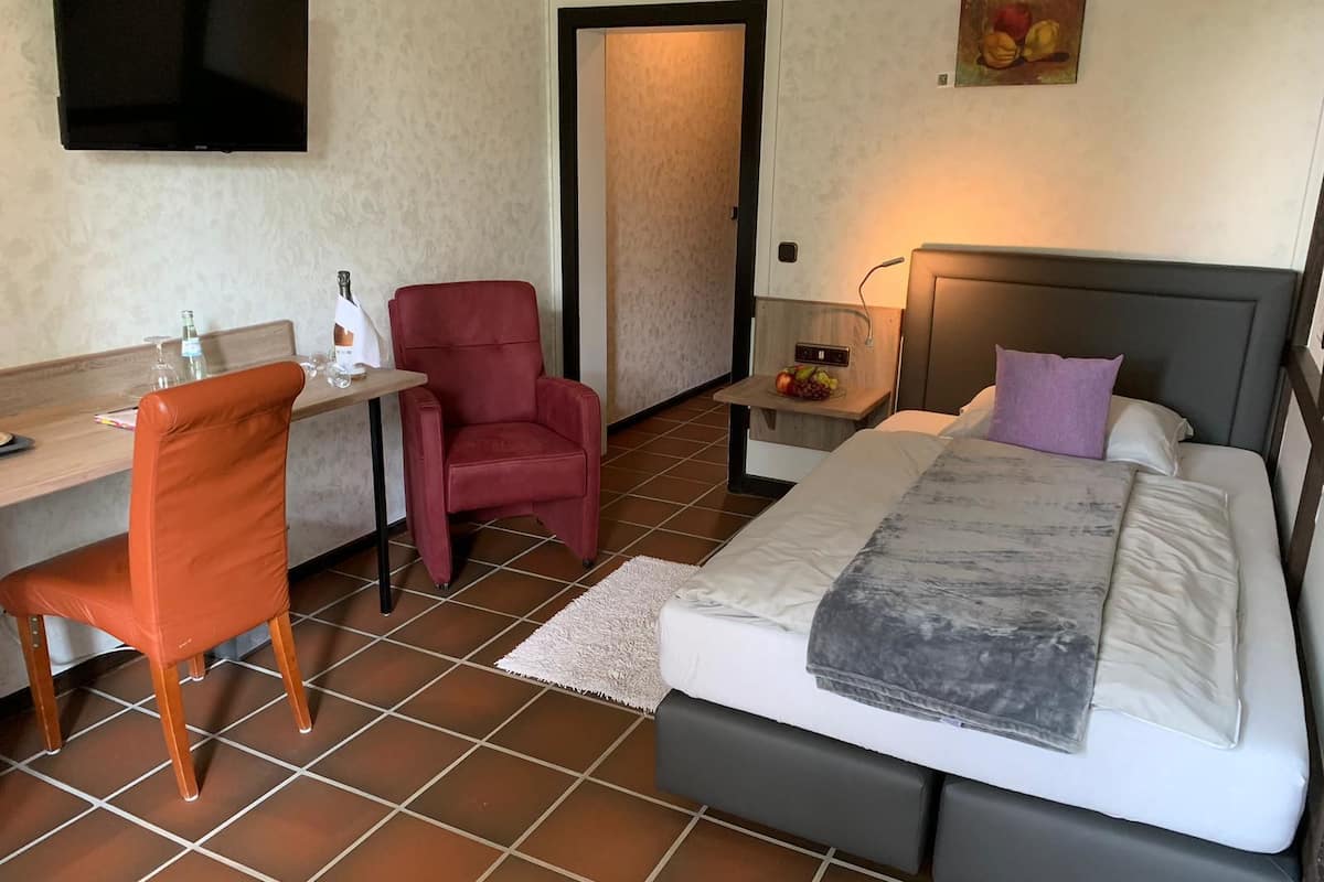 A hotel room with a bed, a desk, a chair, a TV, and a door.