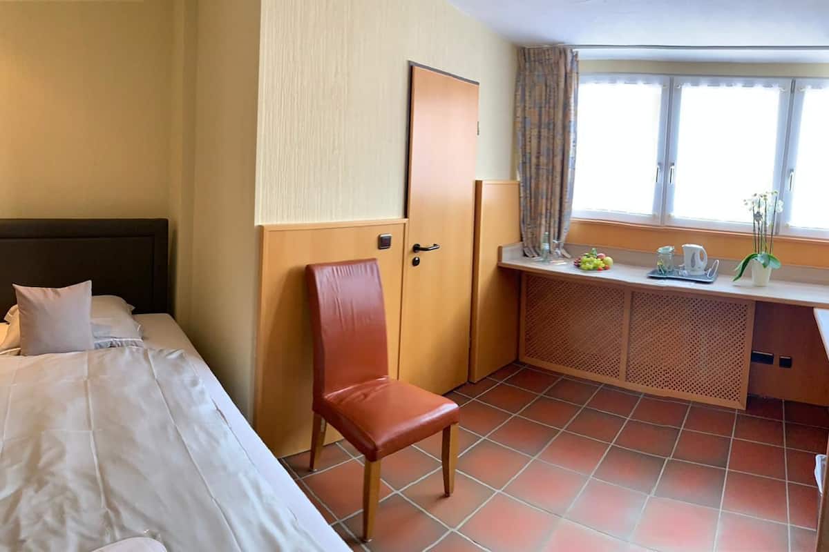A hotel room with a bed, a chair, a desk with a computer, and a window with curtains.