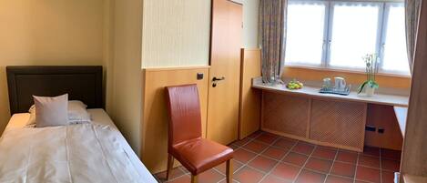 A hotel room with a bed, a chair, a desk with a computer, and a window with curtains.
