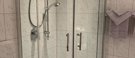 Ducha en esquina con puertas de vidrio, un lavamanos blanco y un perchero.