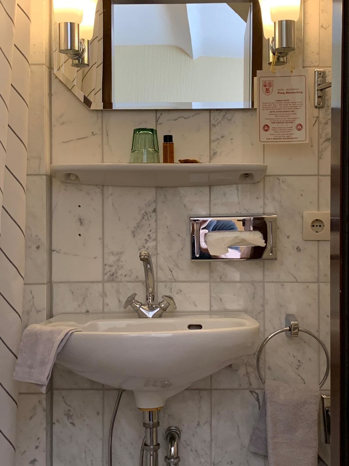 A bathroom with a sink, mirror, towel rack, and a shelf with toiletries.