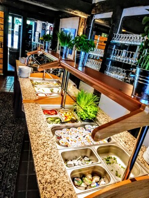 A buffet area with various food stations, including a salad bar and a yogurt bar, with stainless steel serving dishes and a wooden bar counter. - Hotel Burg Wassenberg (Wassenberg)