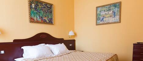 A hotel room with a bed, two paintings on the walls, a nightstand, and a lamp.