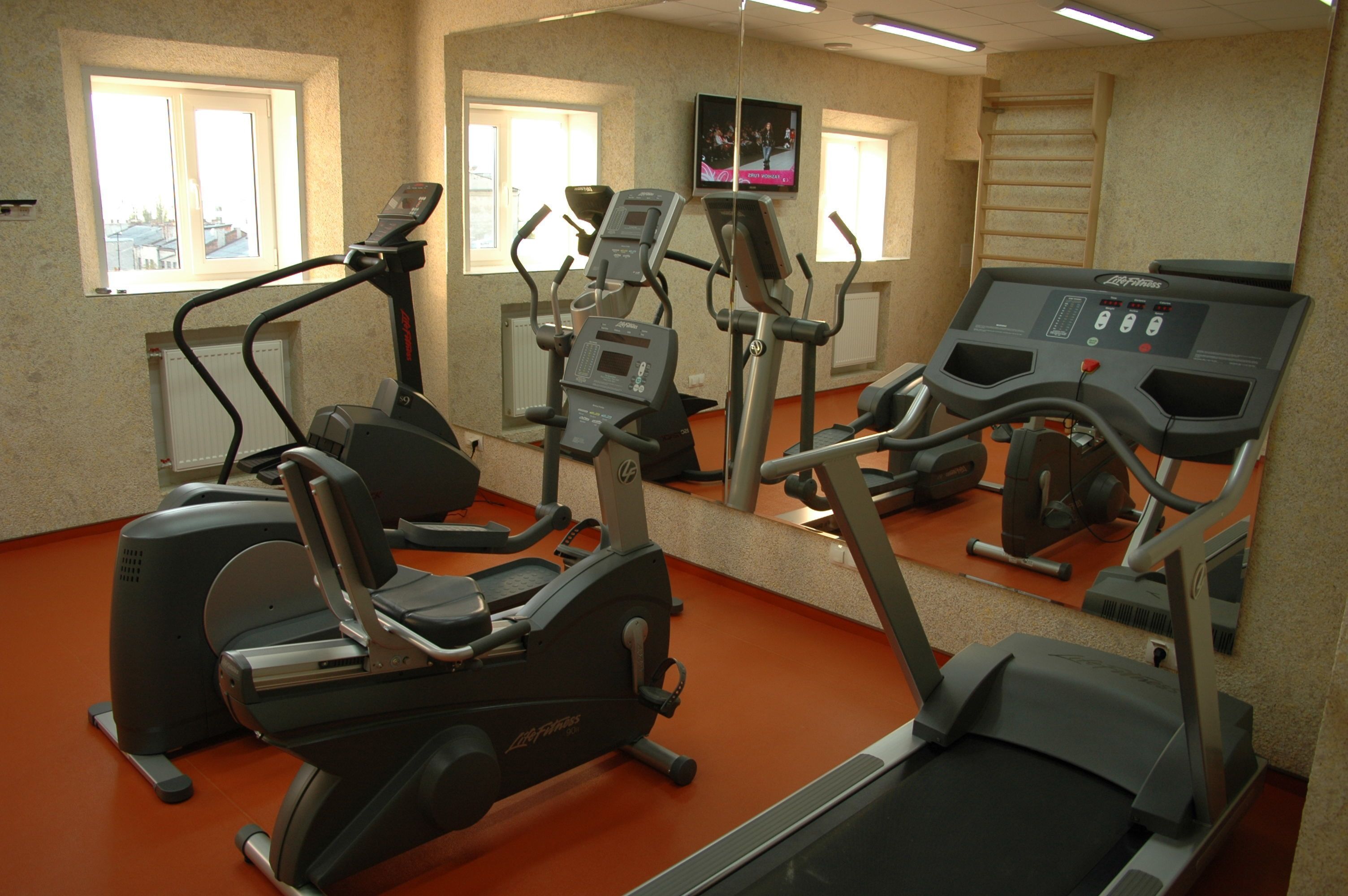 A gym with multiple treadmills, ellipticals, and a TV screen displaying a sports event.