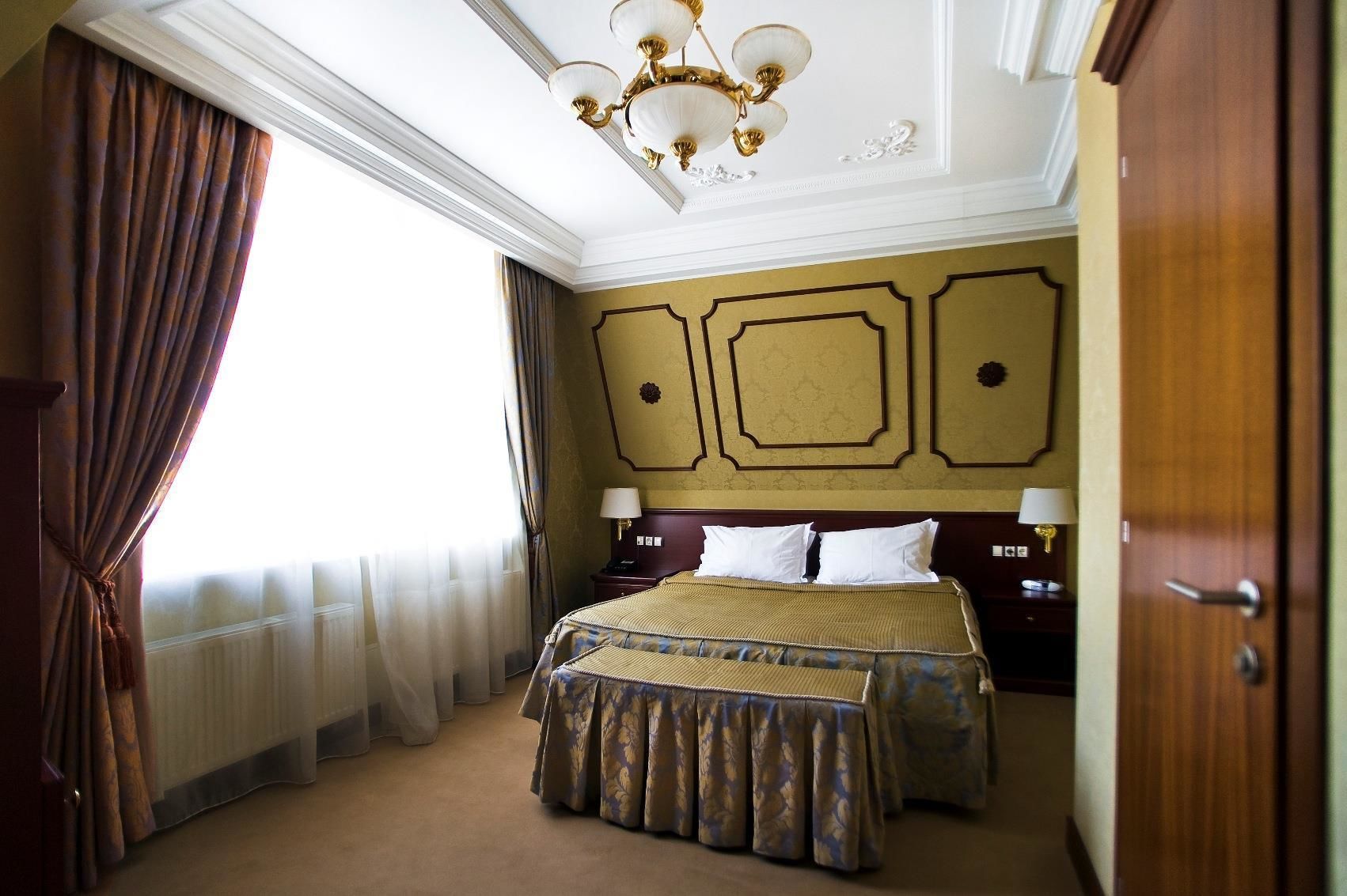 A hotel room with a large bed, a chandelier, and a view of the outdoors.