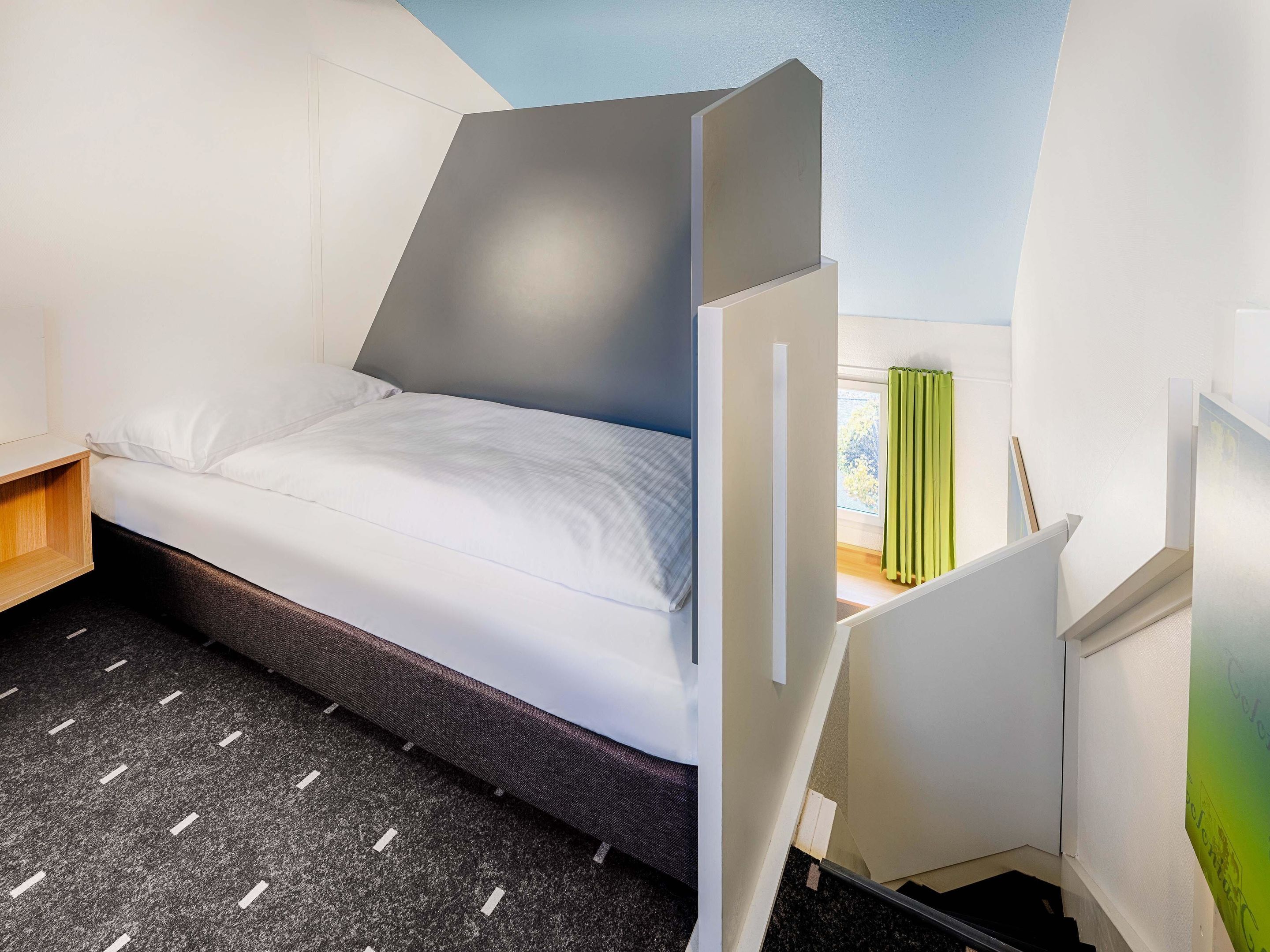 A modern hotel room with a bed, a desk, and a window with curtains.
