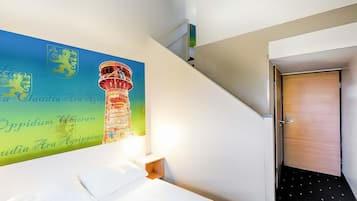 A hotel room with a bed, a nightstand, a wall-mounted lamp, and a door leading to a hallway.