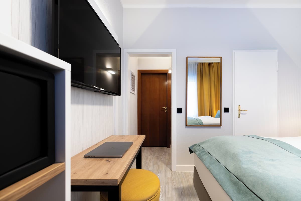 Ein Hotelzimmer mit Bett, Schreibtisch, Laptop, Fernseher und Spiegel.
