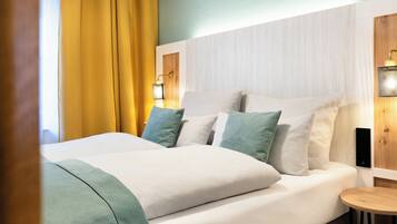 A neatly made bed with white and green bedding, a wooden bedside table, and a wall-mounted light fixture.
