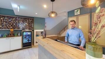Zona de recepción con mostrador de madera, vitrina de vidrio con varios objetos, refrigerador y una escalera al fondo.