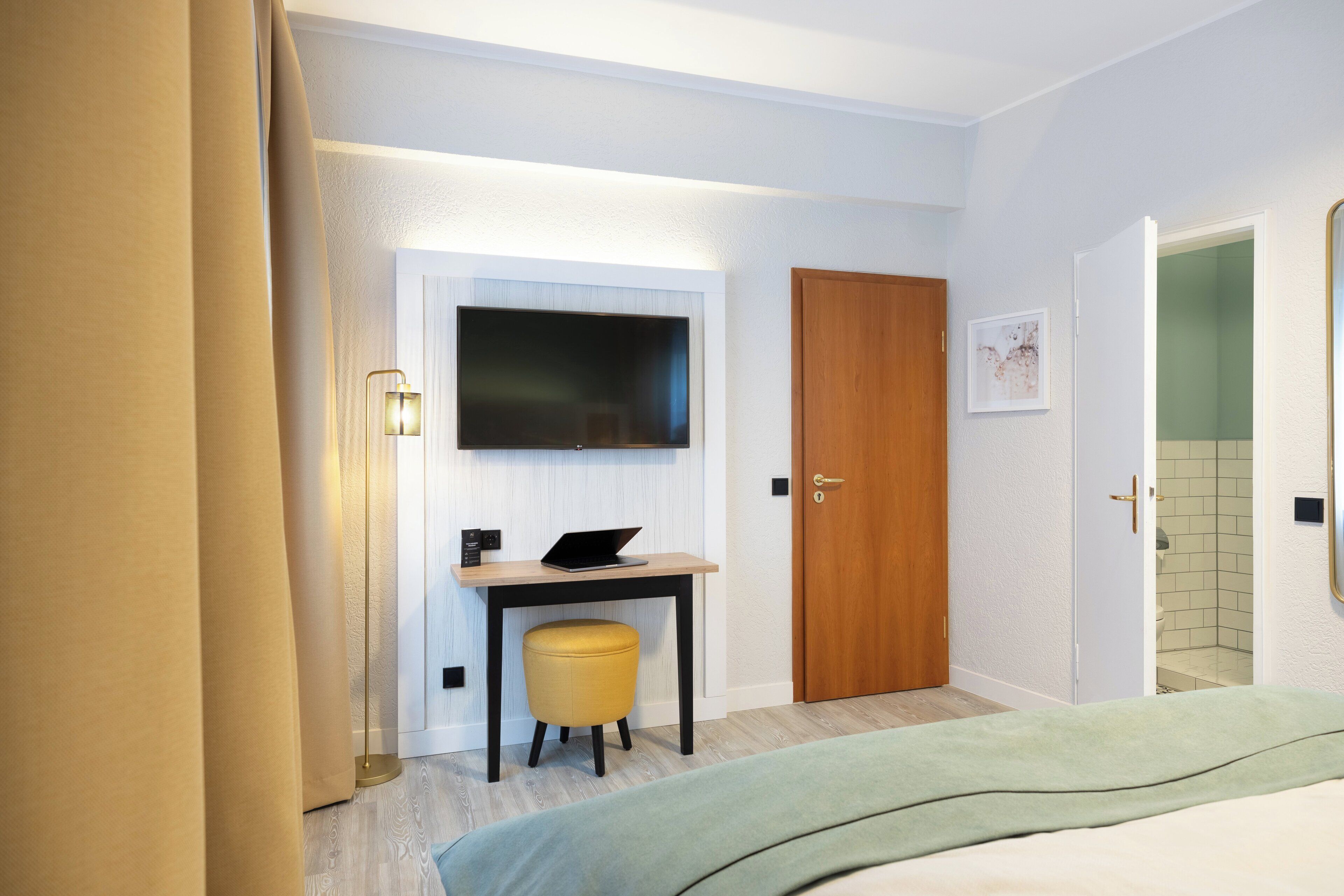 A hotel room with a bed, a desk with a laptop, a television, and a door.