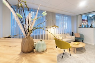 Una sala moderna con una mesa de centro de madera, un sillón amarillo, un sofá y un jarrón con ramas y calabazas.