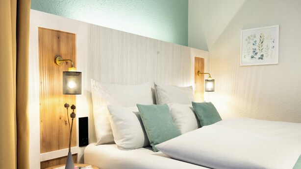 A modern hotel room with a neatly made bed, a small bedside table with a lamp, and a wall-mounted artwork. - Garner Hotel Cologne Engelbertz by IHG (Cologne)