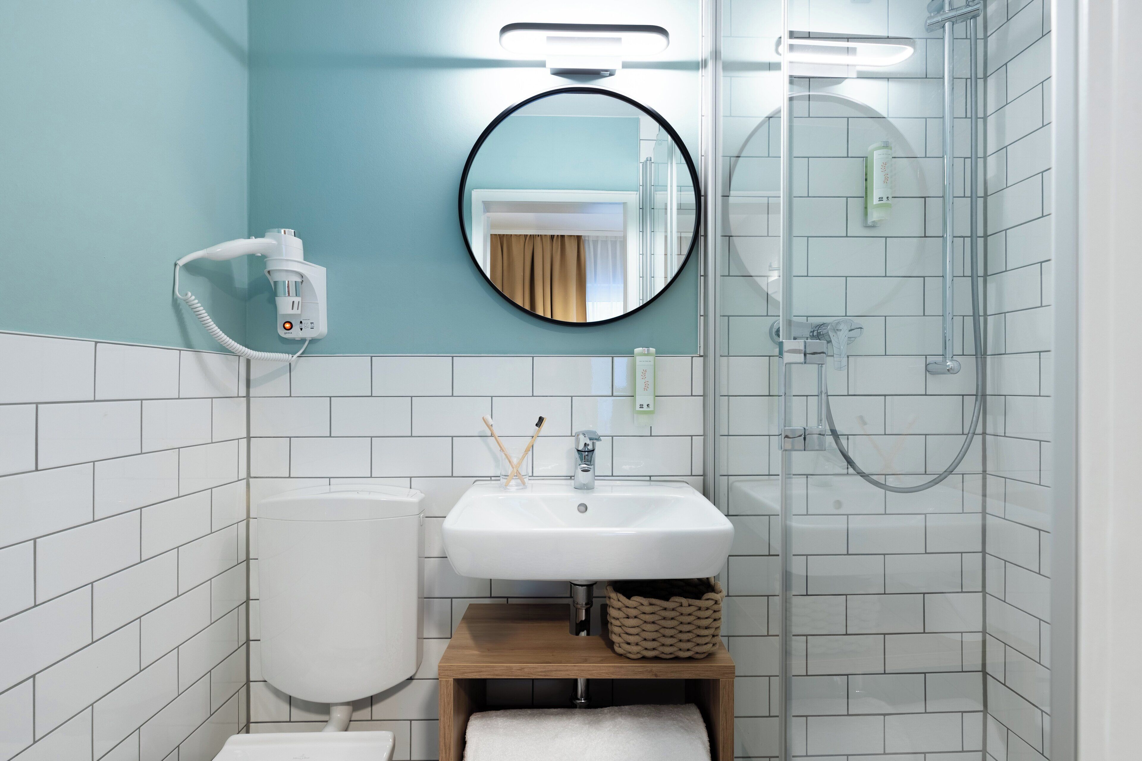 A bathroom with a white sink, a toilet, a round mirror, and a glass-enclosed shower.
