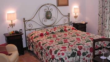 Un dormitorio con colcha estampada de flores, dos lámparas de noche, un cuadro enmarcado en la pared y una silla en la esquina.