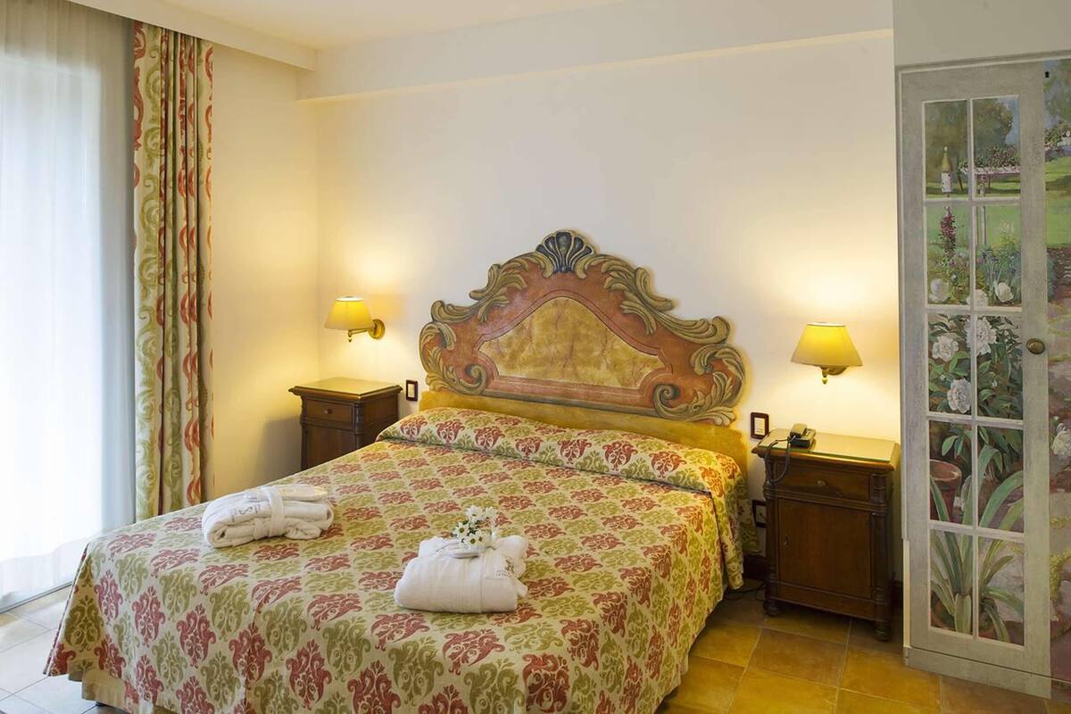 Une chambre d’hôtel avec un grand lit, deux tables de chevet, une tête de lit décorative et une fenêtre avec des rideaux.