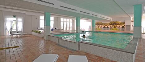 An indoor swimming pool with tiled floors and white lounge chairs.