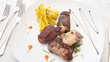 A plate with grilled meat, fries, and a sauce, accompanied by a fork and knife on a table.