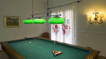 A pool table with balls, a chair, and a painting on the wall.