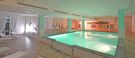 A large indoor swimming pool with lounge chairs and a waterfall mural.