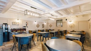 A restaurant with round tables and chairs, a bar area, and a high ceiling with exposed beams. - Logis Hôtel la Grassinais Saint-Malo (Saint-Malo)