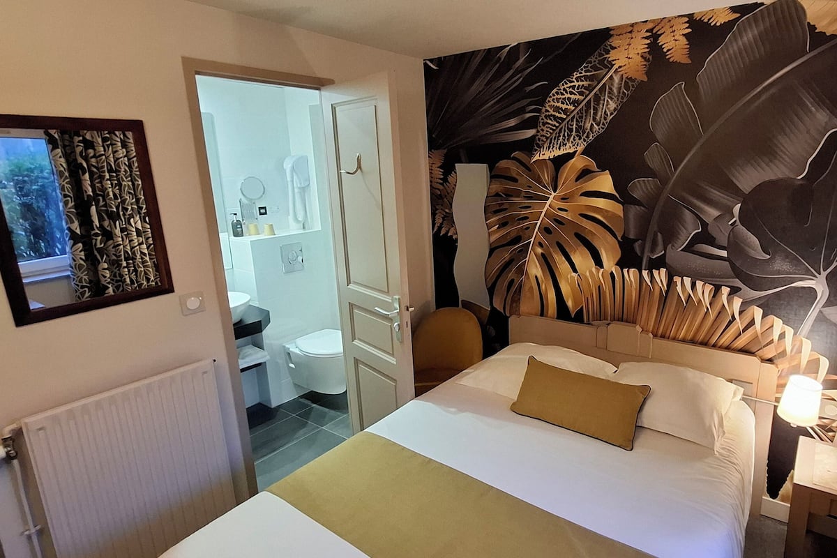 A bedroom with a bed, a nightstand, a large wall mural, and a bathroom visible through an open door.