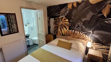 Une chambre à coucher avec un lit, une table de chevet, une grande fresque murale et une salle de bain visible à travers une porte ouverte.