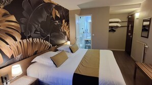 A hotel room with a large bed, a nightstand, a desk, and a bathroom visible through an open door. - Logis Hôtel la Grassinais Saint-Malo (Saint-Malo)