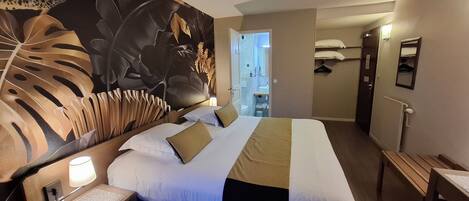 Quarto de hotel com uma cama grande, mesa de cabeceira, escrivaninha e casa de banho visível por uma porta aberta.