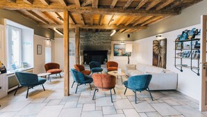 A modern interior with a stone fireplace, wooden ceiling beams, and a variety of seating options including sofas and chairs. - Logis Hôtel la Grassinais Saint-Malo (Saint-Malo)
