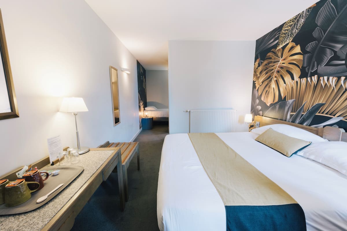 A hotel room with a bed, bedside table, lamp, and a large tropical leaf painting on the wall.