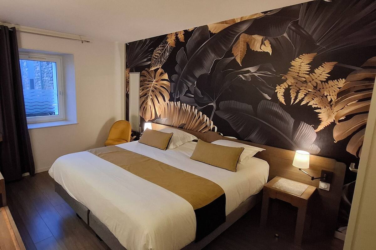 A hotel room with a large bed, a television, a desk with a lamp, and a window with curtains.