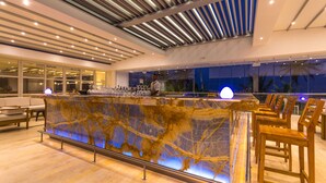 A modern bar area with a marble countertop, seating, and a ceiling with linear lighting.