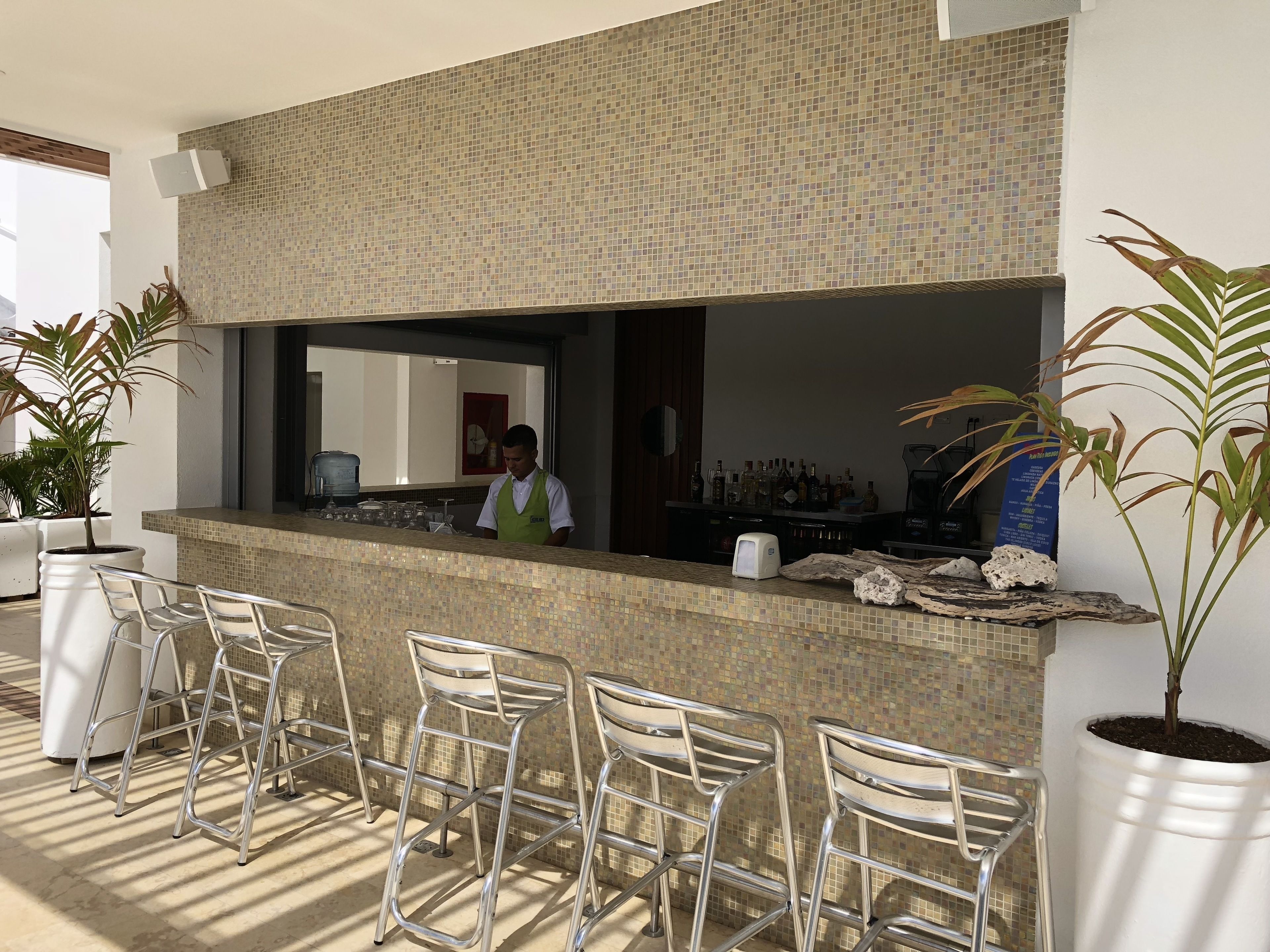 Zona de bar con salpicadero de azulejos, taburetes de metal y un barman.