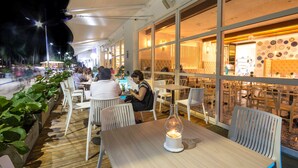 An outdoor dining area with tables and chairs, a candle on one table, and a view of the street in the background.