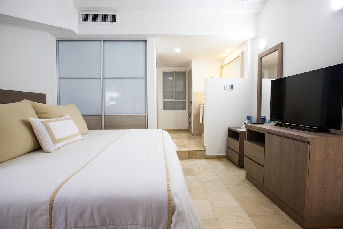 Une chambre d’hôtel avec un grand lit, un téléviseur posé sur une commode en bois et un placard à portes coulissantes.