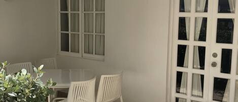 A patio area with a white table and chairs, a potted plant, and a door with multiple windows.