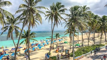 Una playa con palmeras, sombrillas y gente.