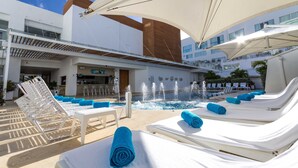 A poolside area with sun loungers, a bar, and a water feature.