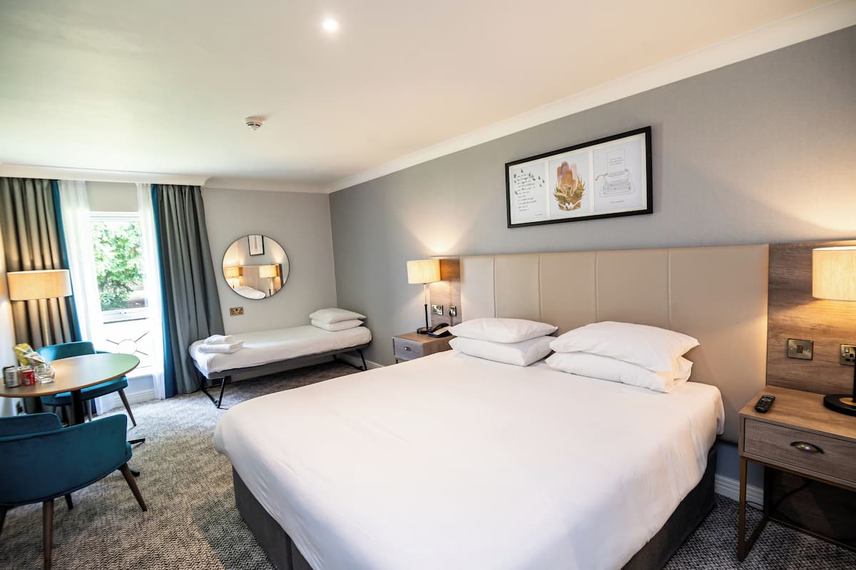 A hotel room with a large bed, two bedside tables, a desk with a chair, and a window with curtains.