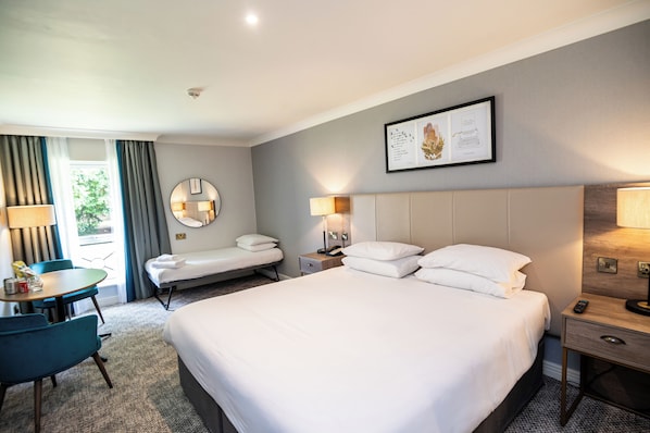 A hotel room with a large bed, two bedside tables, a desk with a chair, and a window with curtains.